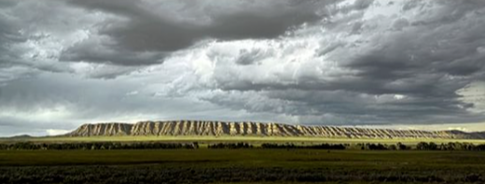 Panoramic landscape photo of badlands in the distance with stormy clouds above.